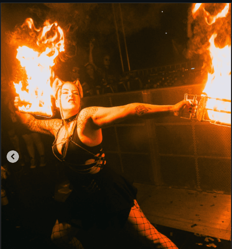 SIN FIRE performer kneeling with flaming torches before an audience