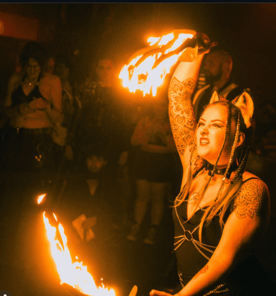 SIN FIRE performer spinning a flaming fire fan with audience behind