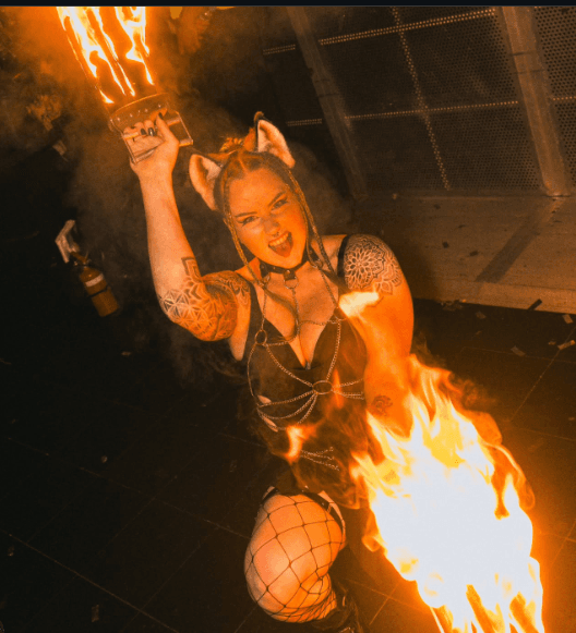 SIN FIRE performer posed beside a large flame on the floor