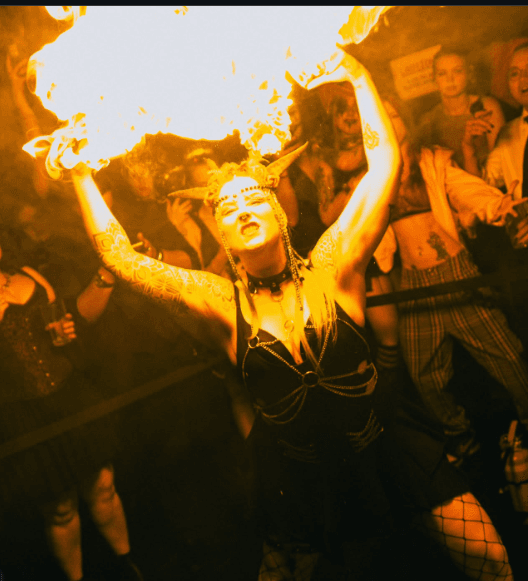 SIN FIRE performer breathing a wide plume of fire toward the ceiling